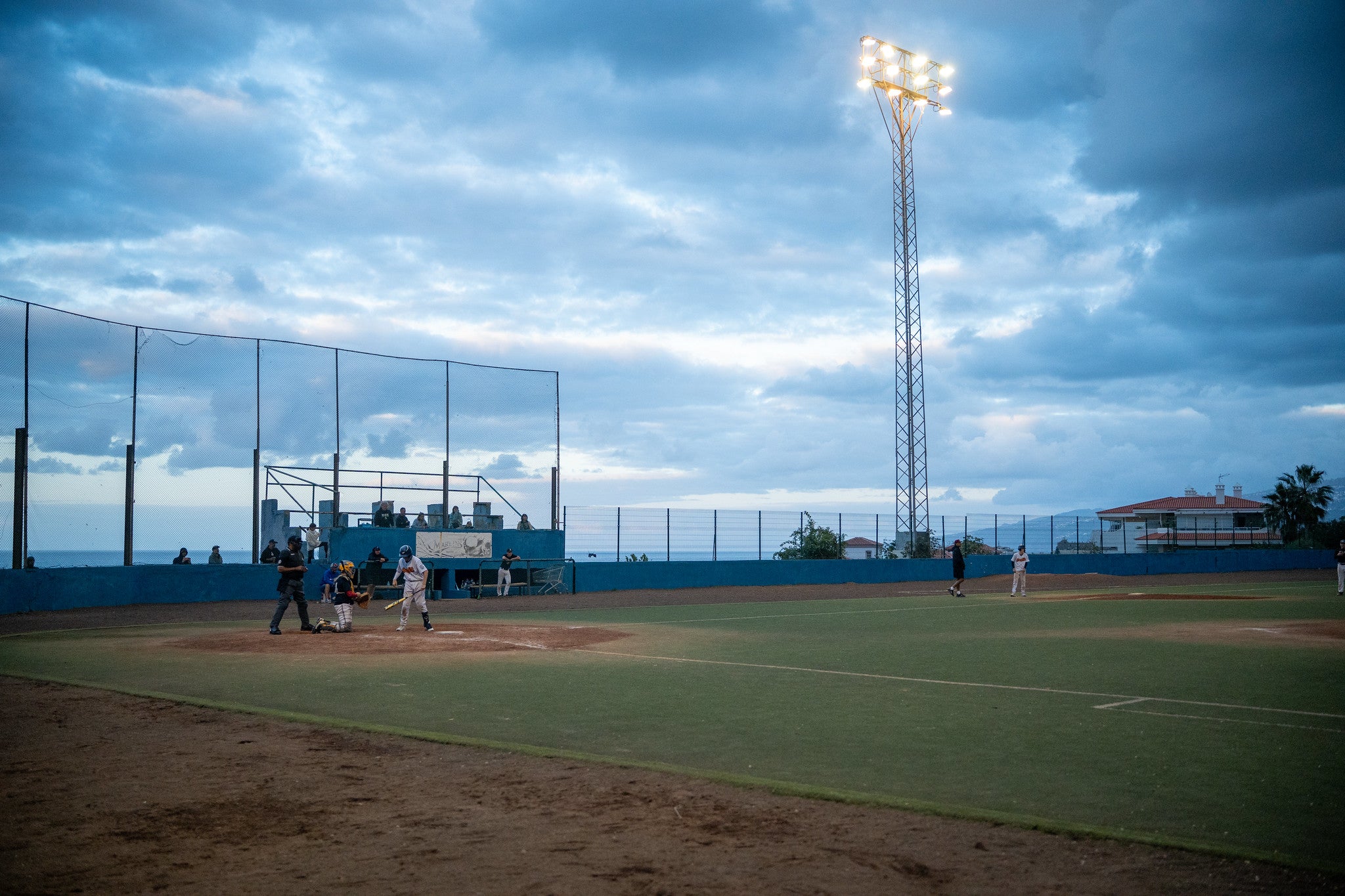 Baseballspiel auf einem Außenfeld bei Flutlicht mit Blick auf das Spielfeld und Himmel
