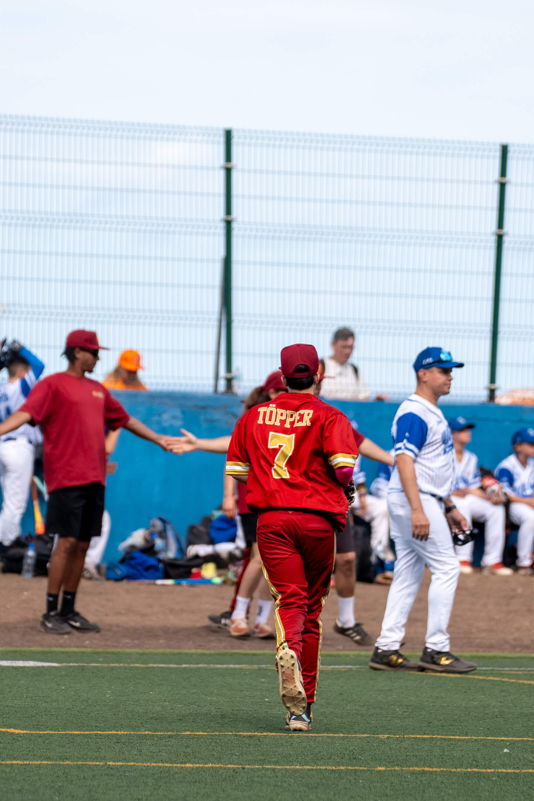 U13-Baseballspieler in roter Uniform mit der Rückennummer 7 läuft über das Spielfeld, im Hintergrund weitere Spieler und Trainer