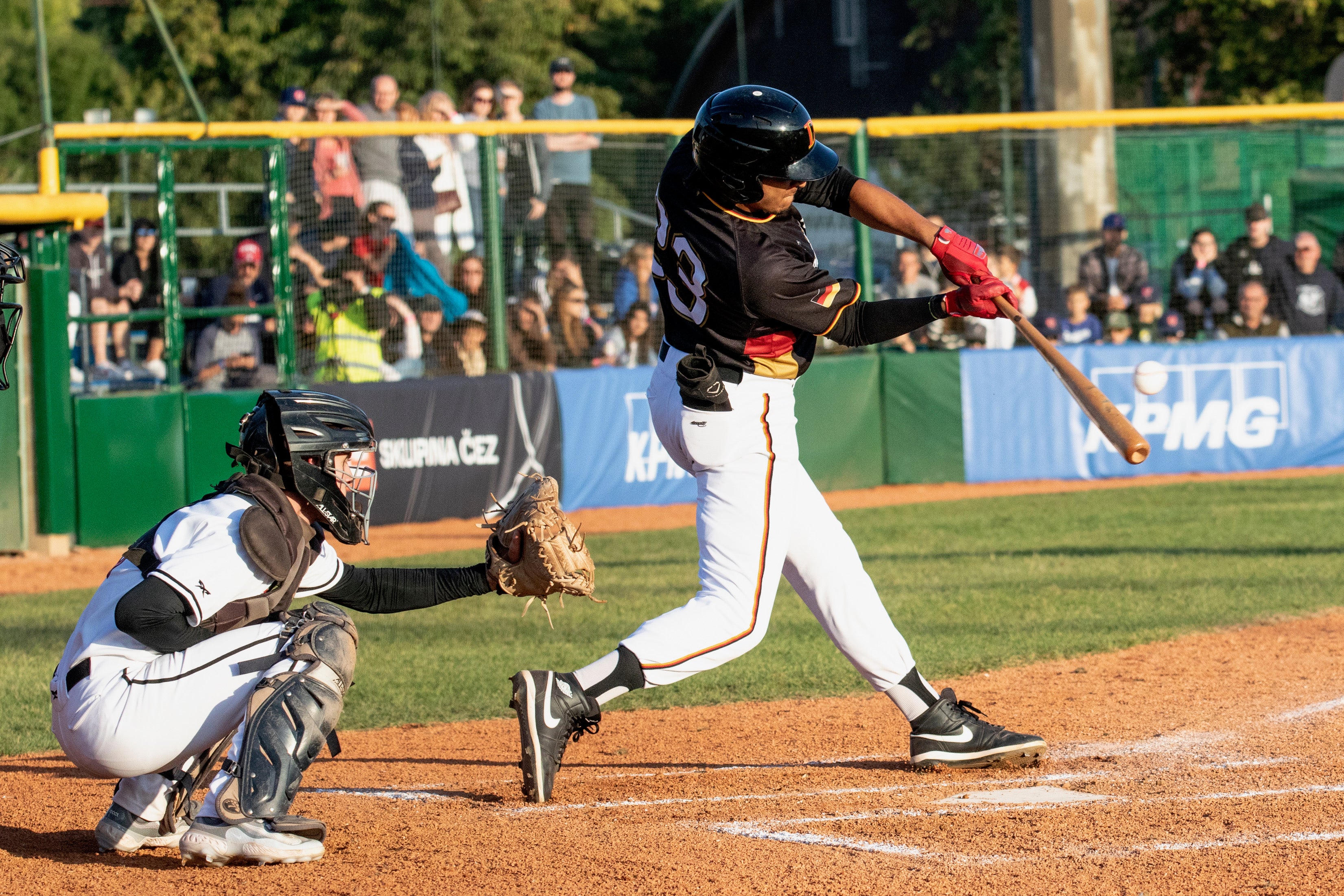 Baseballspieler trifft den Ball mit dem Schläger während eines Spiels, Catcher in Fangposition, Zuschauer im Hintergrund