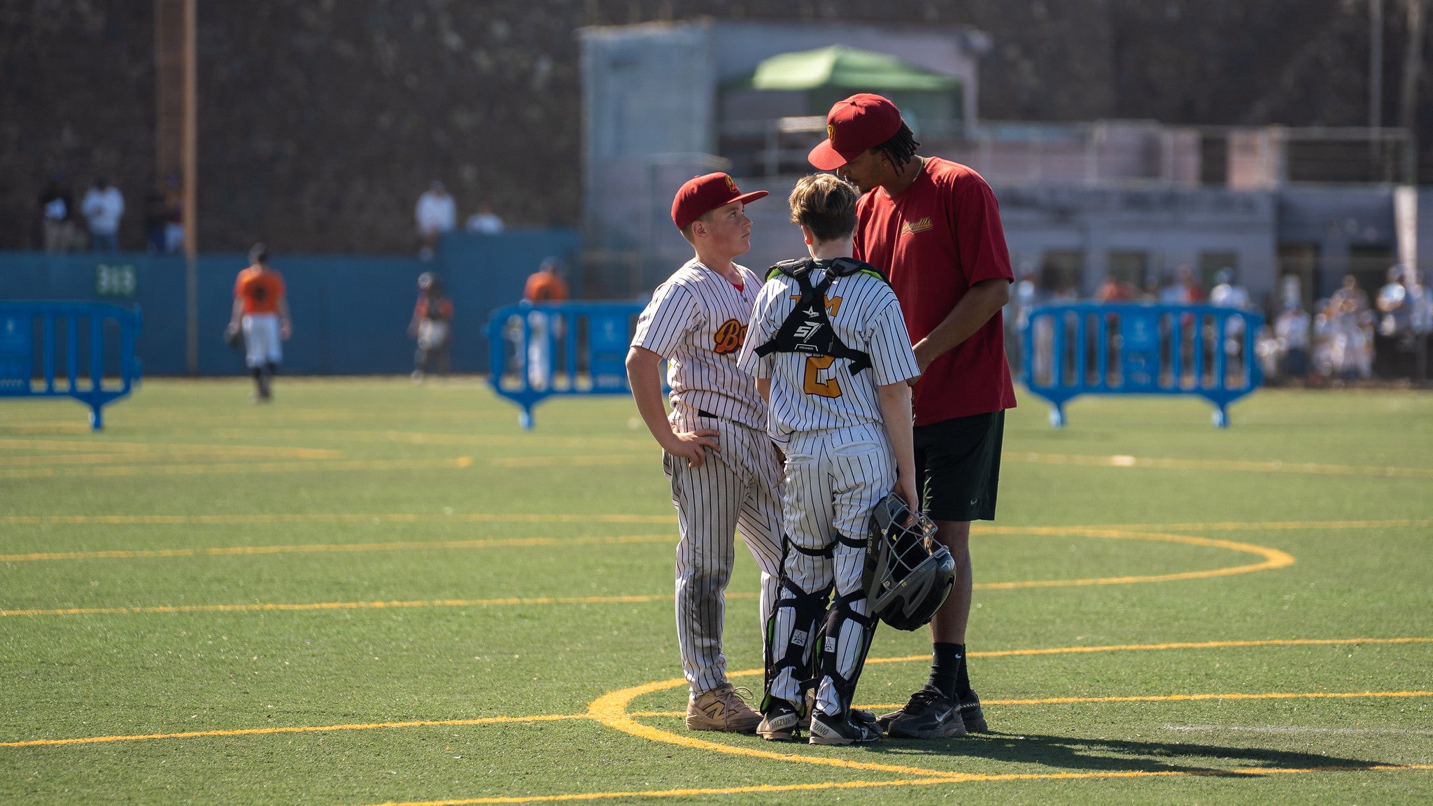 Coach spricht mit zwei U13-Baseballspielern auf dem Spielfeld während einer Spielpause