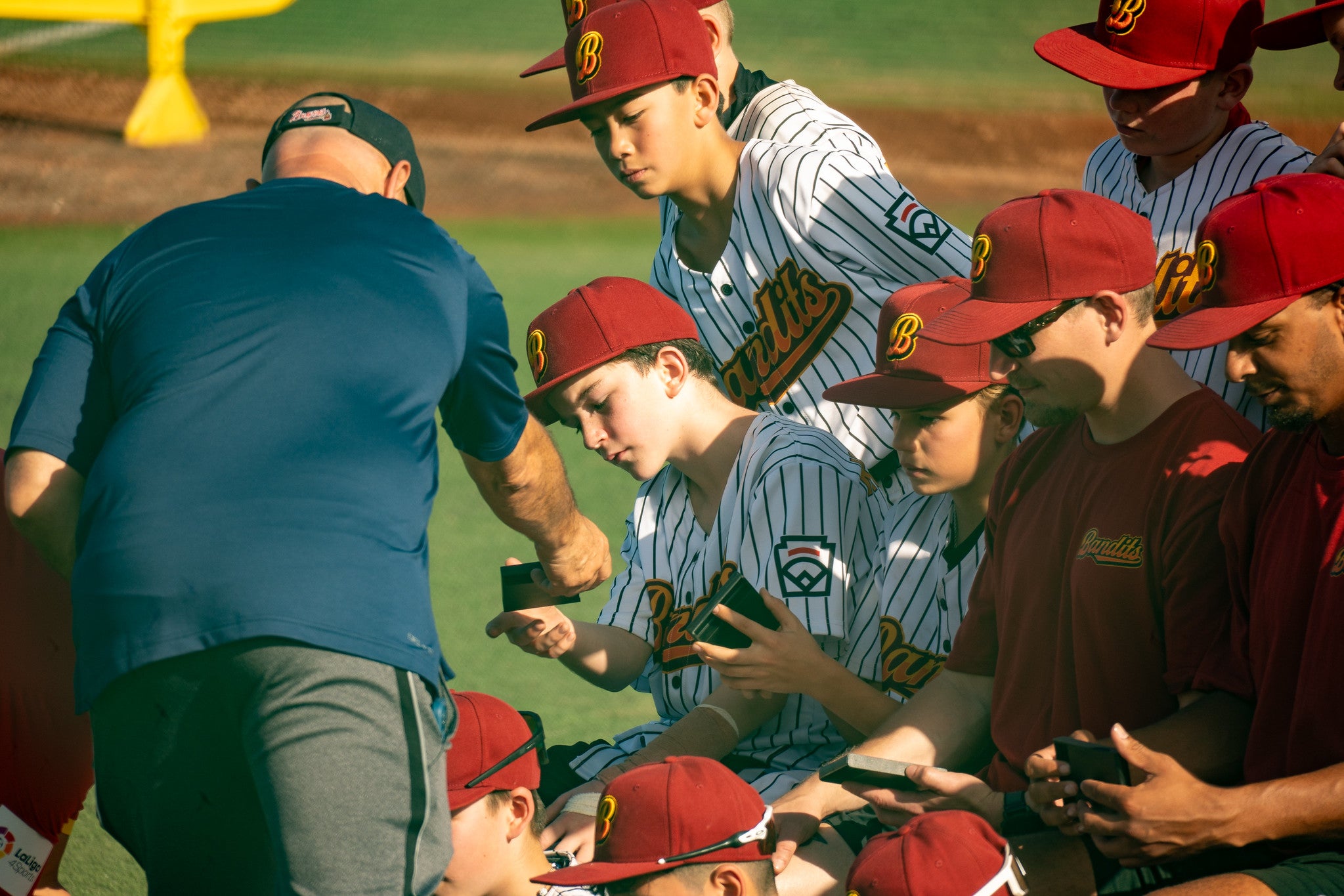 Helfer übergibt Auszeichnungen an U13-Baseballspieler, die auf der Bank zusammensitzen