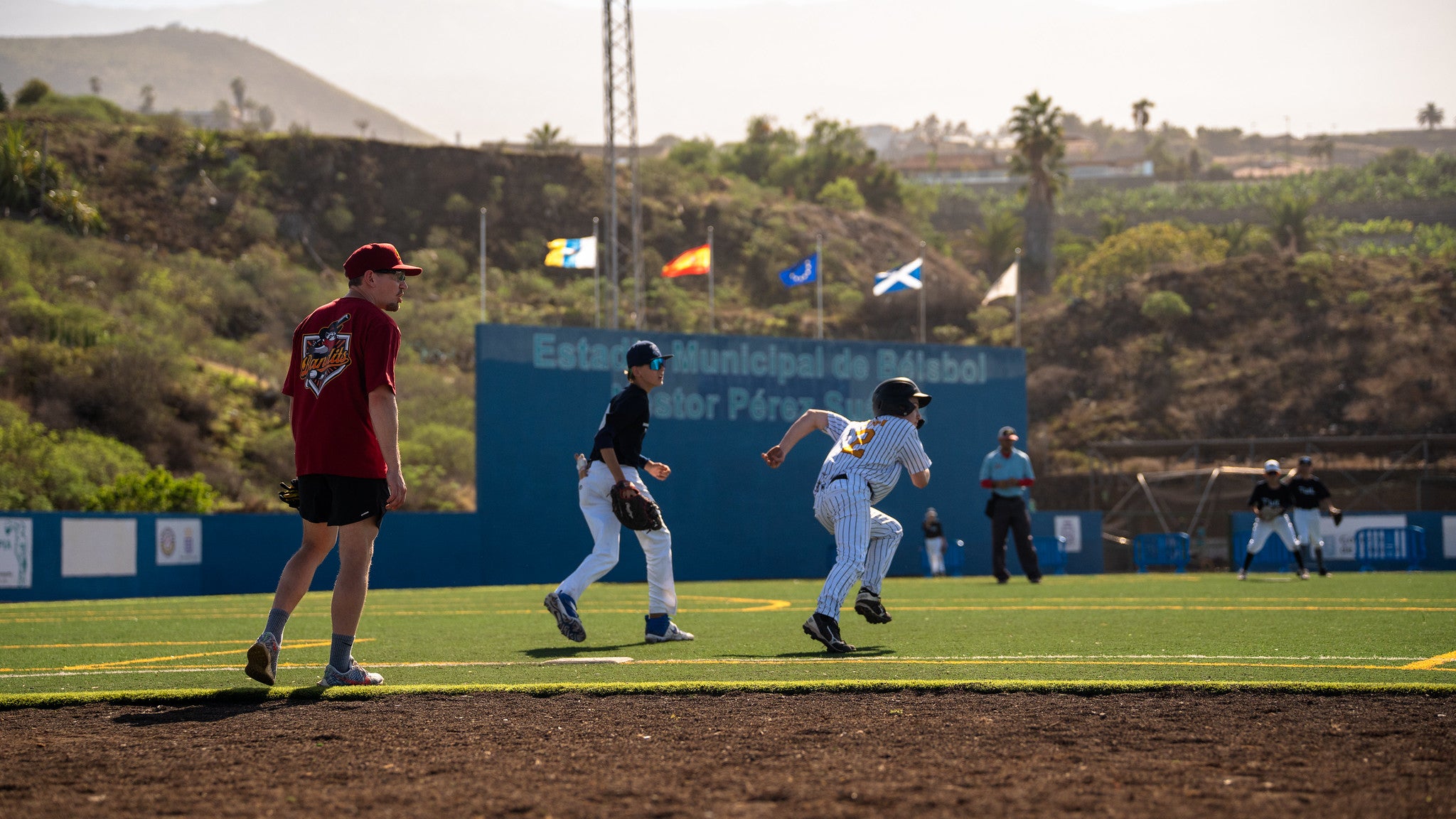 U15-Baseballspieler sprintet im Infield, während Feldspieler und Trainer das Spiel beobachten