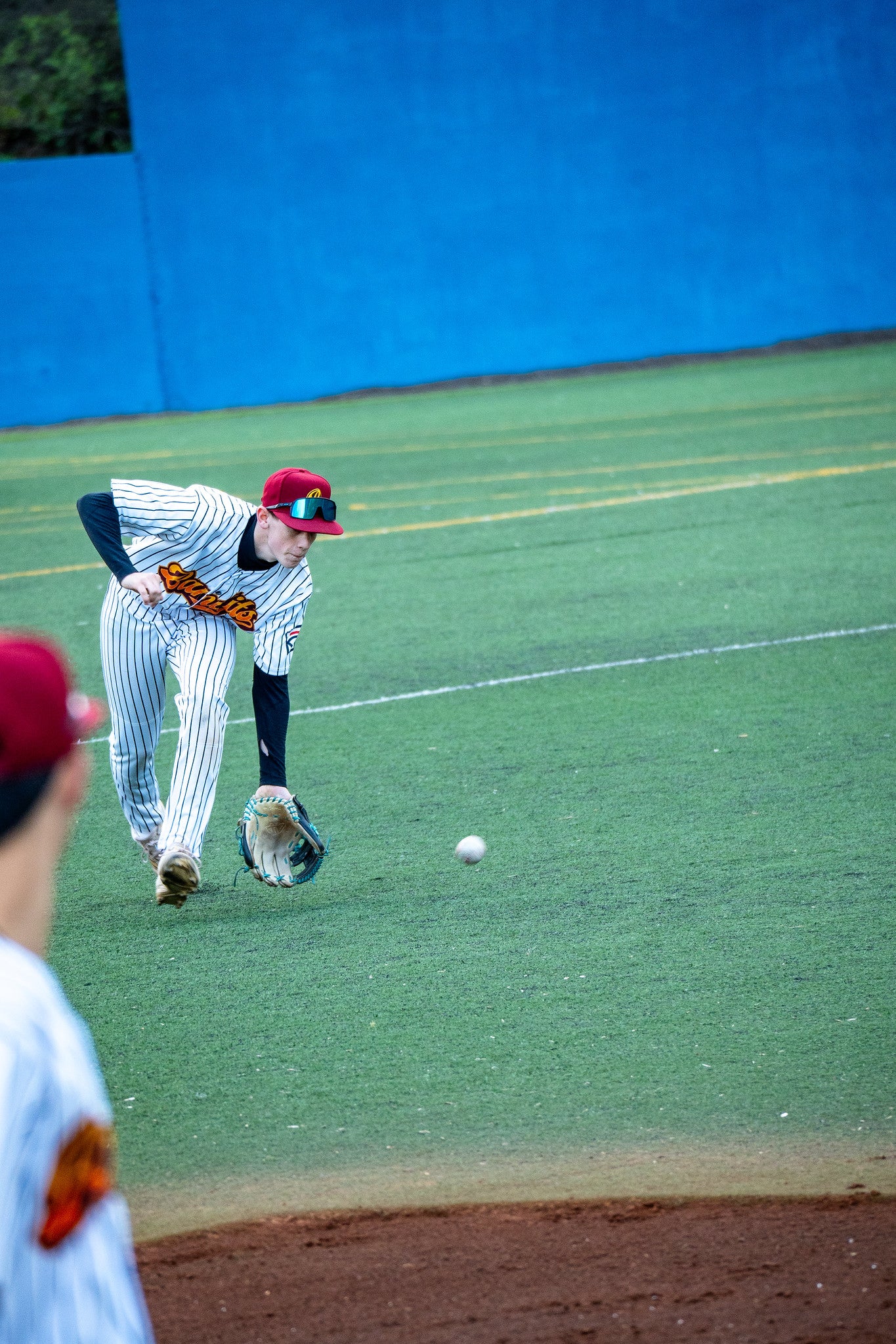 U15-Baseballspieler bewegt sich nach vorne, um einen langsam rollenden Ball im Infield aufzunehmen
